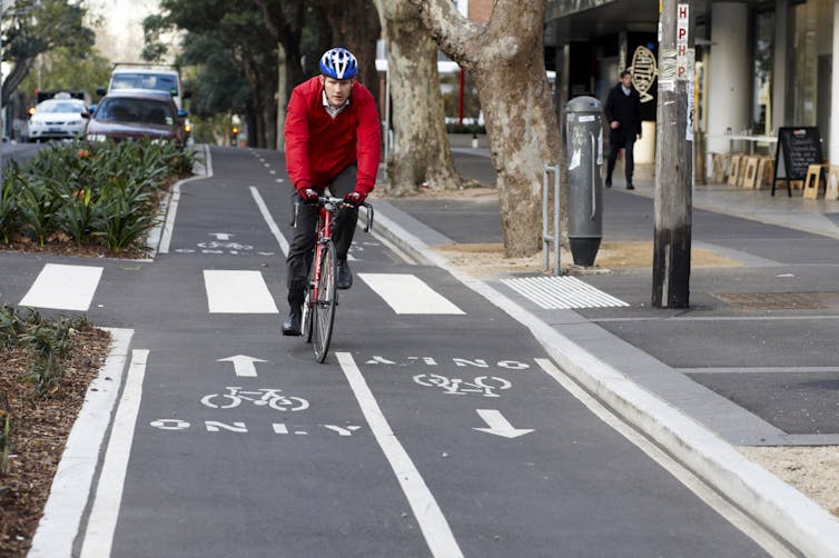 Man in red jumper cycling on bike lane.
