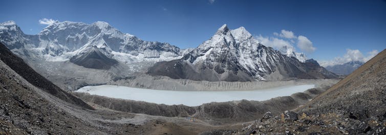 A glacial lake with high peaks behind it shows how dams build up from the glacier's movement