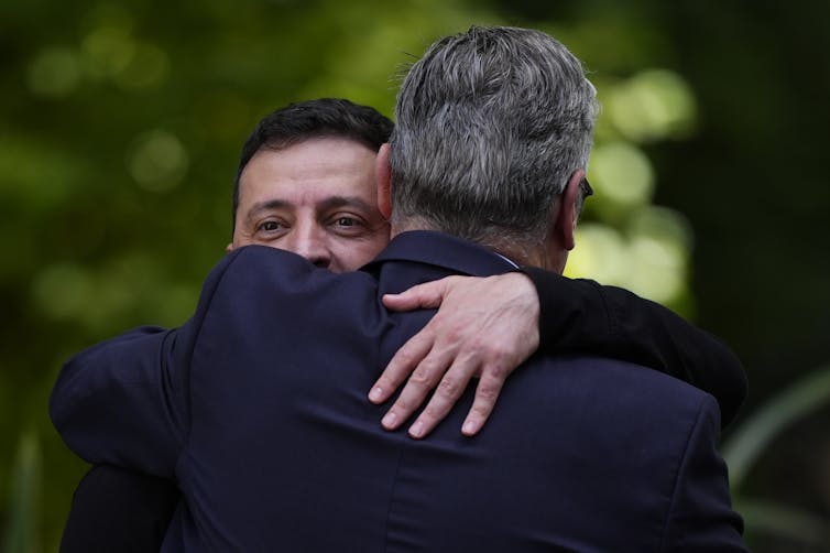 Two men in dark clothes hugging each other.