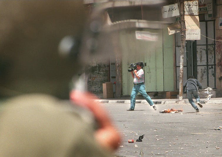 A man is seen in a street holding a video camera.