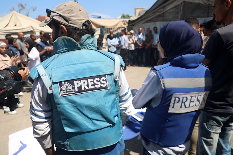 Two Palestinians wearing press insignia stand at the site of the airstrike on Nasser hospital.