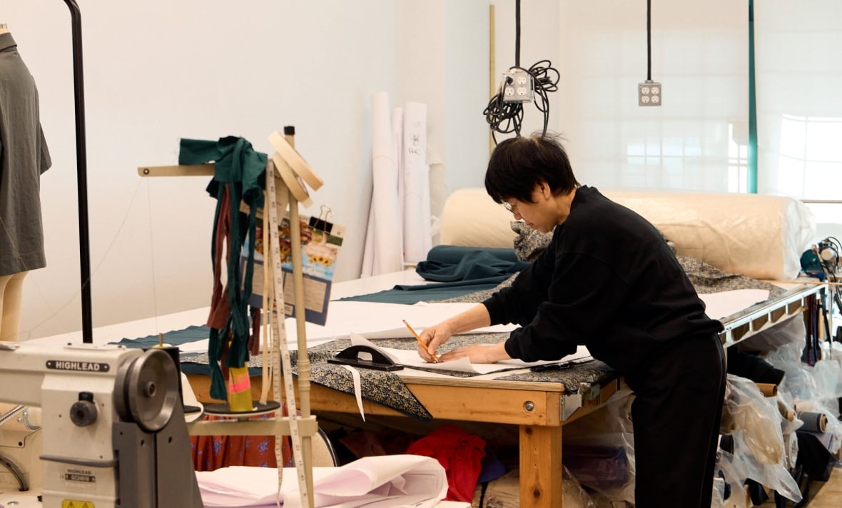 A woman uses a pencil and paper to trace a pattern over a garment on a table.