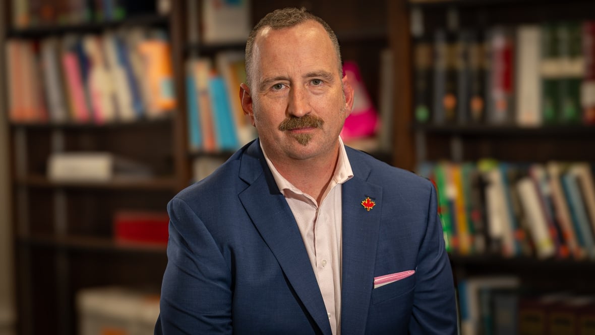 Headshot of man in suit with books in the background. 
