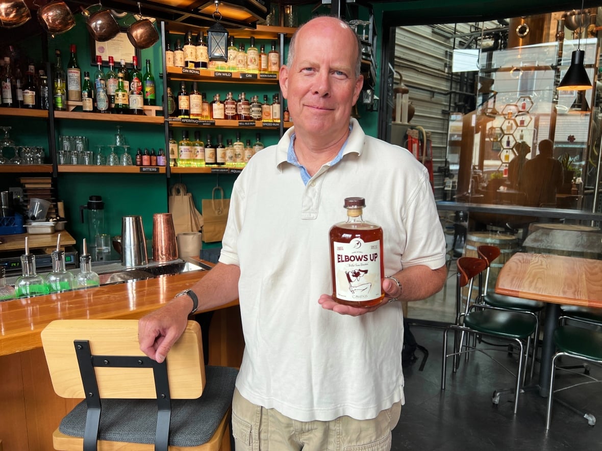 A bald, white man wearing a golf shirt holds a bottle of alcohol manufactured at the facility where he serves as president.