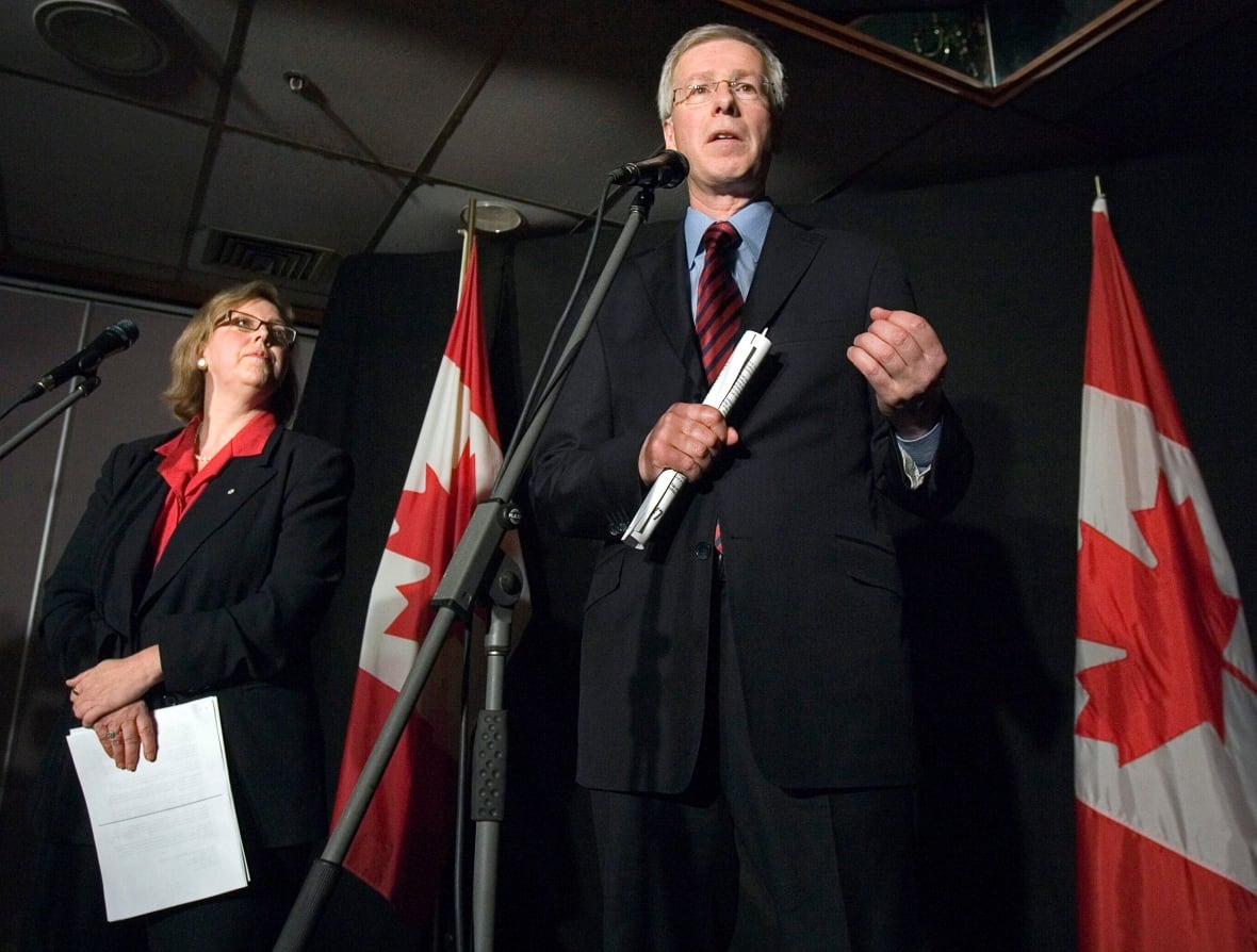 A man speaks into a microphone as a woman watches on.