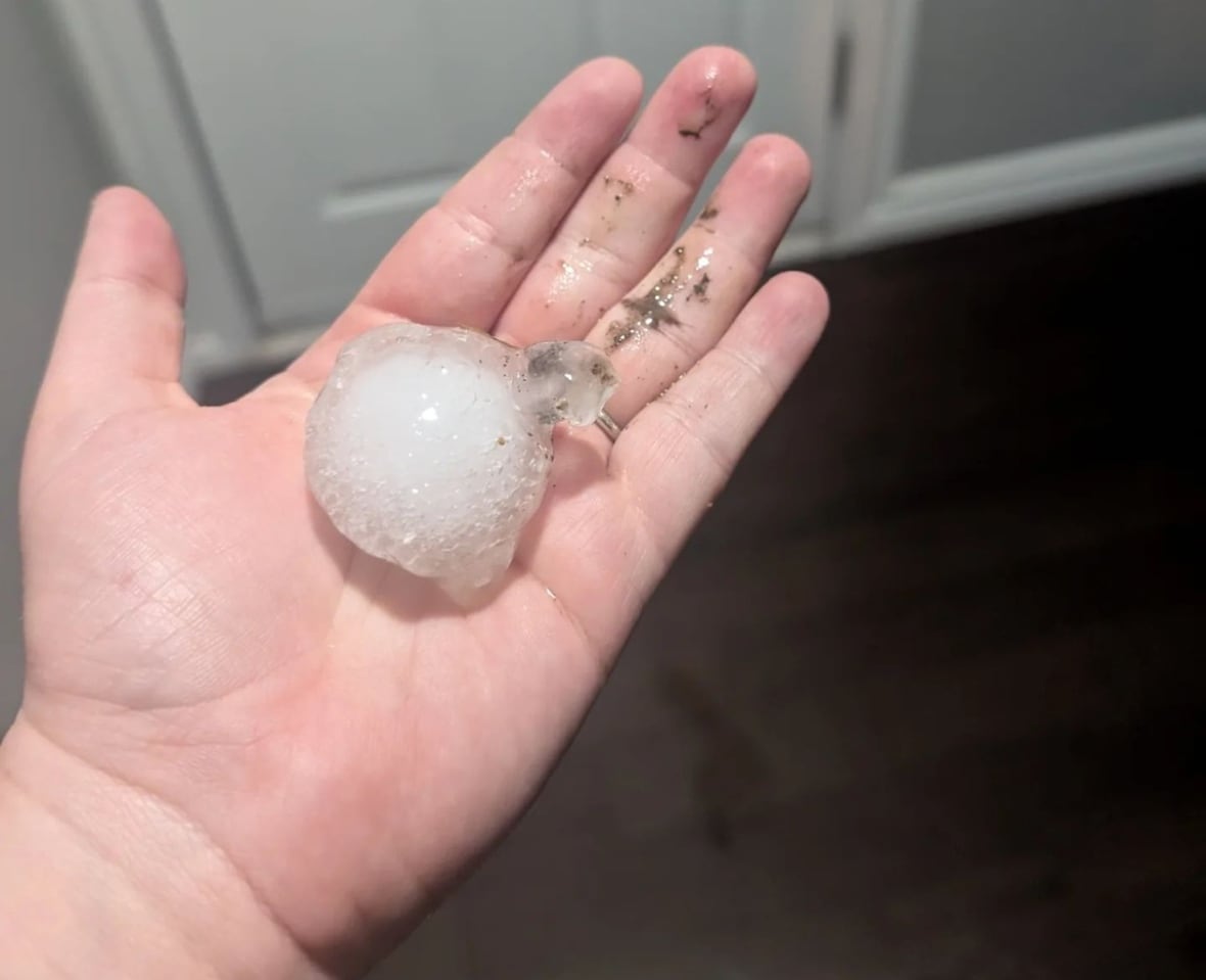 a piece of hail roughly the size of a golf ball sits in a woman's hand.