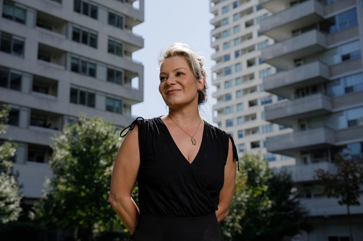 A woman stands on the street, two residential buildings behind her.