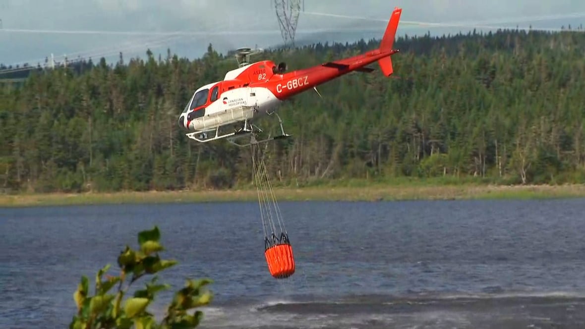 A helicopter over a body of water with a bucket.