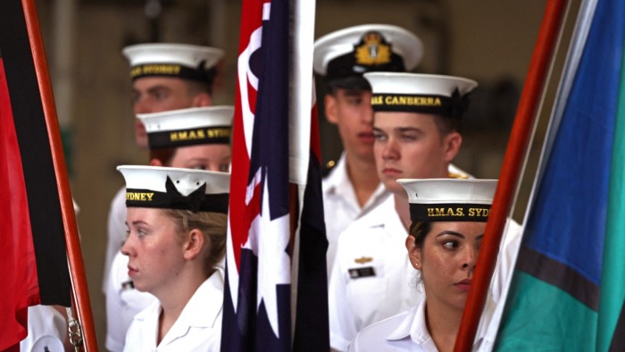 Sailors from the Royal Australian Navy stand behind flags aboard the Australian Navy ship HMAS Canberra