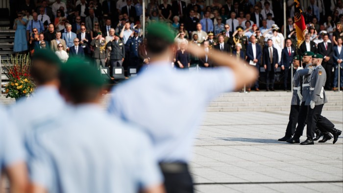 Soldiers in uniform carry a German flag during an oath-taking ceremony in Berlin as a crowd watches and salutes.