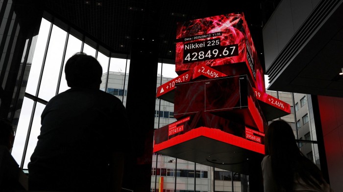 People watch a large electronic display showing the Nikkei 225 index at 42,849.67 points