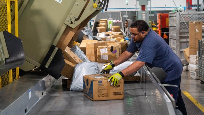 A USPS worker wearing gloves sorts packages on a conveyor belt at a mail processing centre during the holiday season