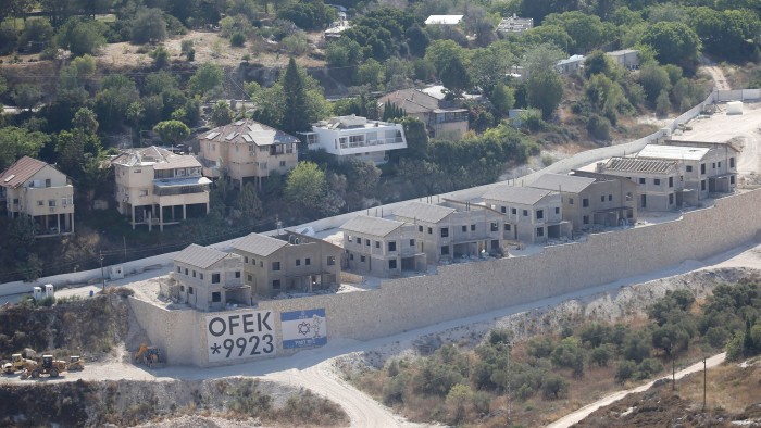 A row of unfinished buildings in the Jewish settlement of Kadim, with construction vehicles and a large sign on a stone wall in front.