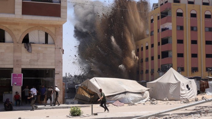 People run for cover as a large explosion sends smoke and debris into the air near tents and buildings in Jabalia, Gaza Strip.