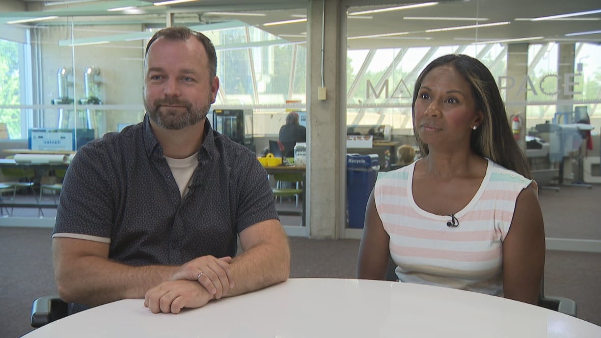 A man, left, and woman are seated at a table next to each other at a public library.