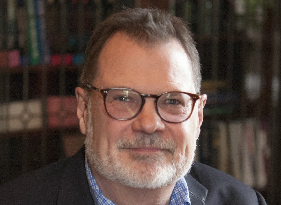 A man with glasses and a greying goatee smiles while posing for a portrait. 