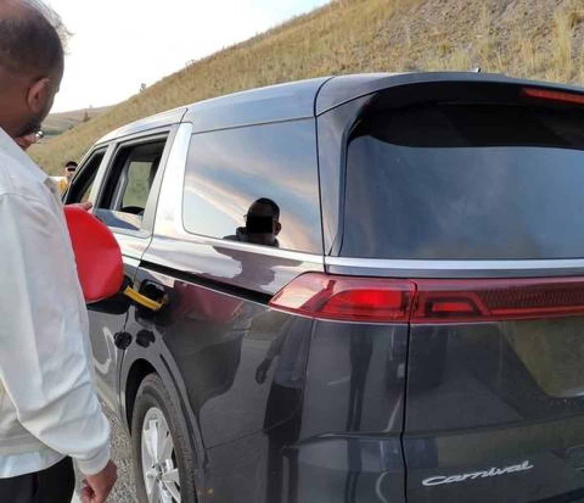 A person refuels a grey SUV with a red jerry can.