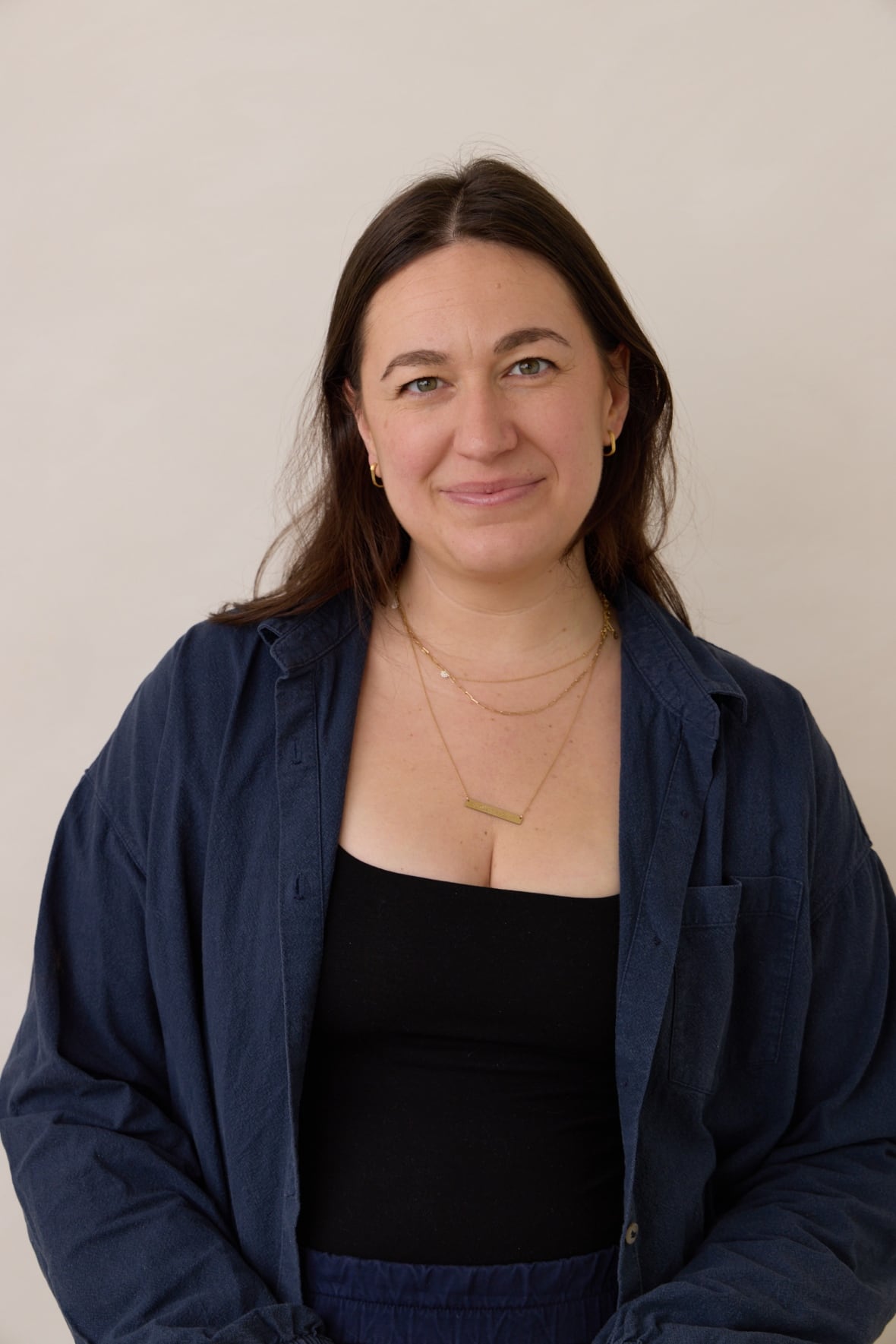 A woman wearing a black shirt and a blue overcoat is pictured.