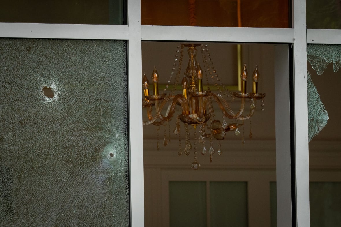 Bullet holes are pictured in the windows of a cafe, with a chandelier in the background.