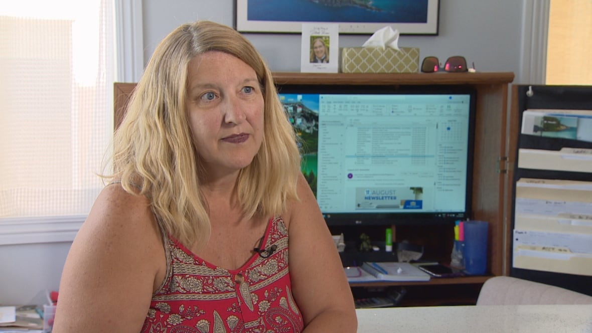 A woman with blonde hair and a red tank top sits in front of a computer.