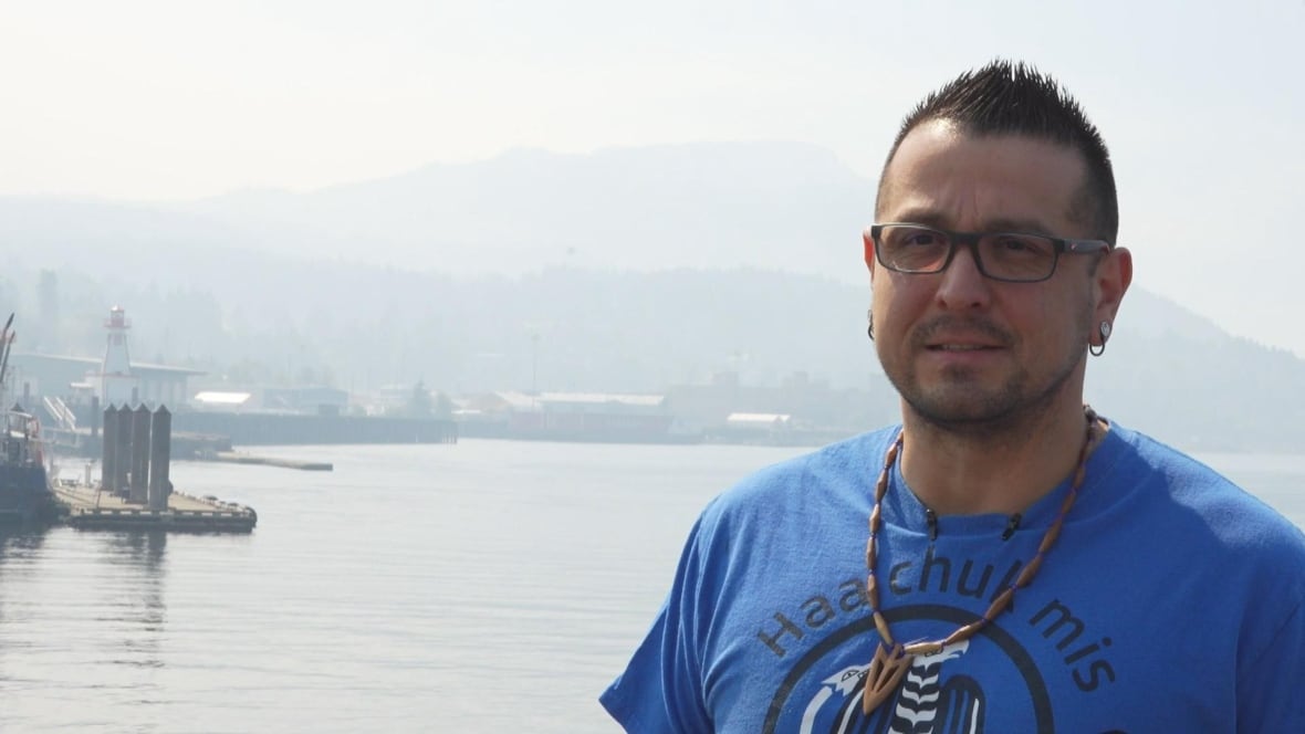 A man wearing a blue T-shirt is seen with a smoky marina behind him.