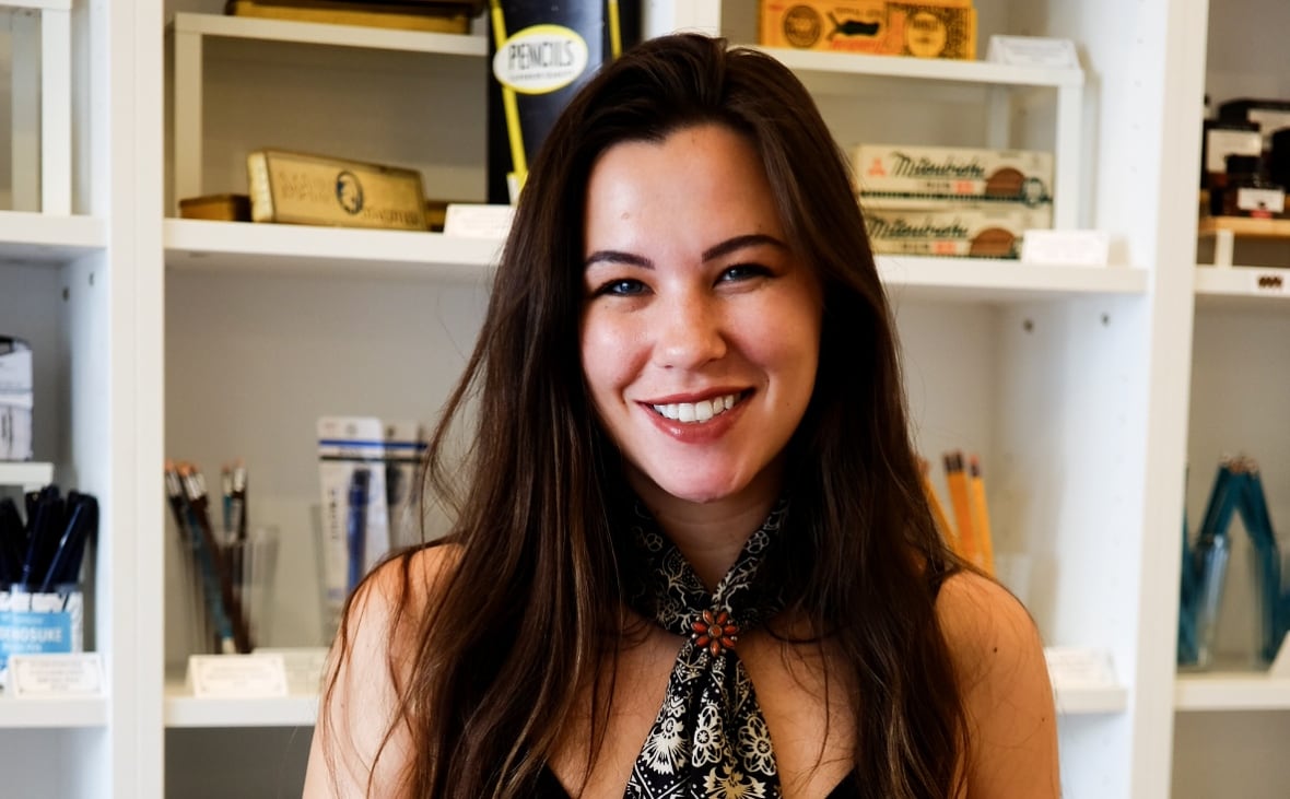A woman with long, dark hair smiles while posing for a photo in front of a white bookshelf. 