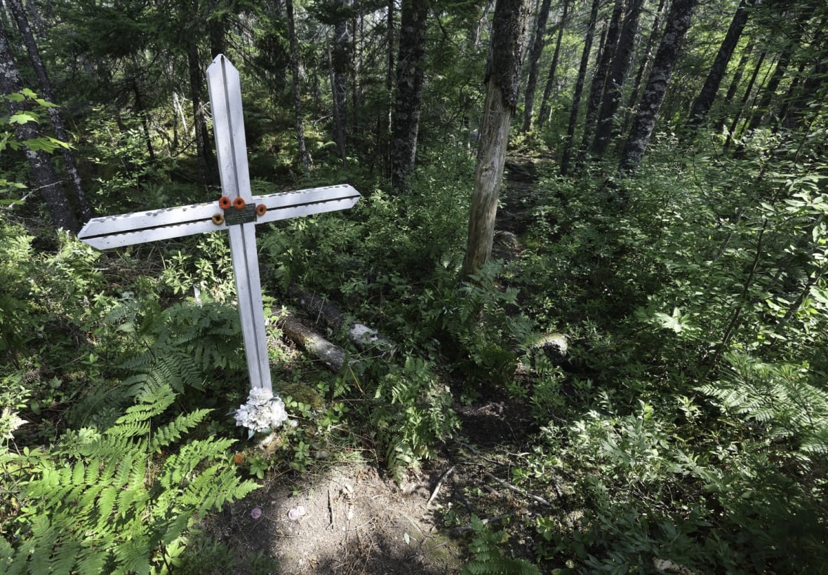 A white cross with a plaque sits in a wooded area.