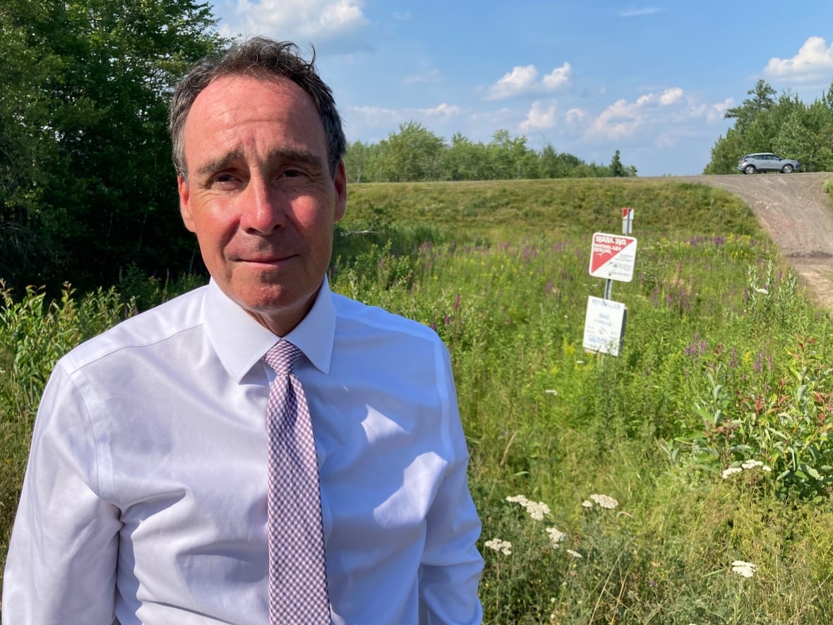 A man with a white dress shirt and purple tie looks into the camera.