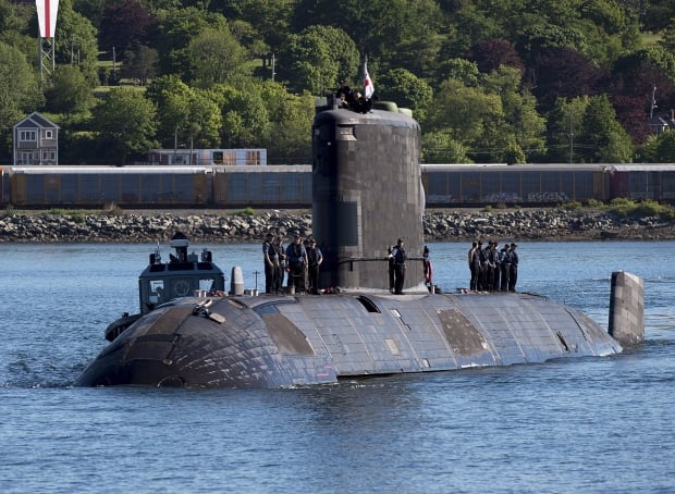 A submarine at the surface of a body of water with people standing on top.