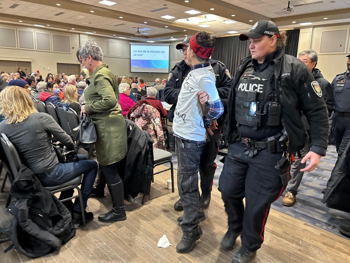 Two police officers escort a protester out of a community meeting.