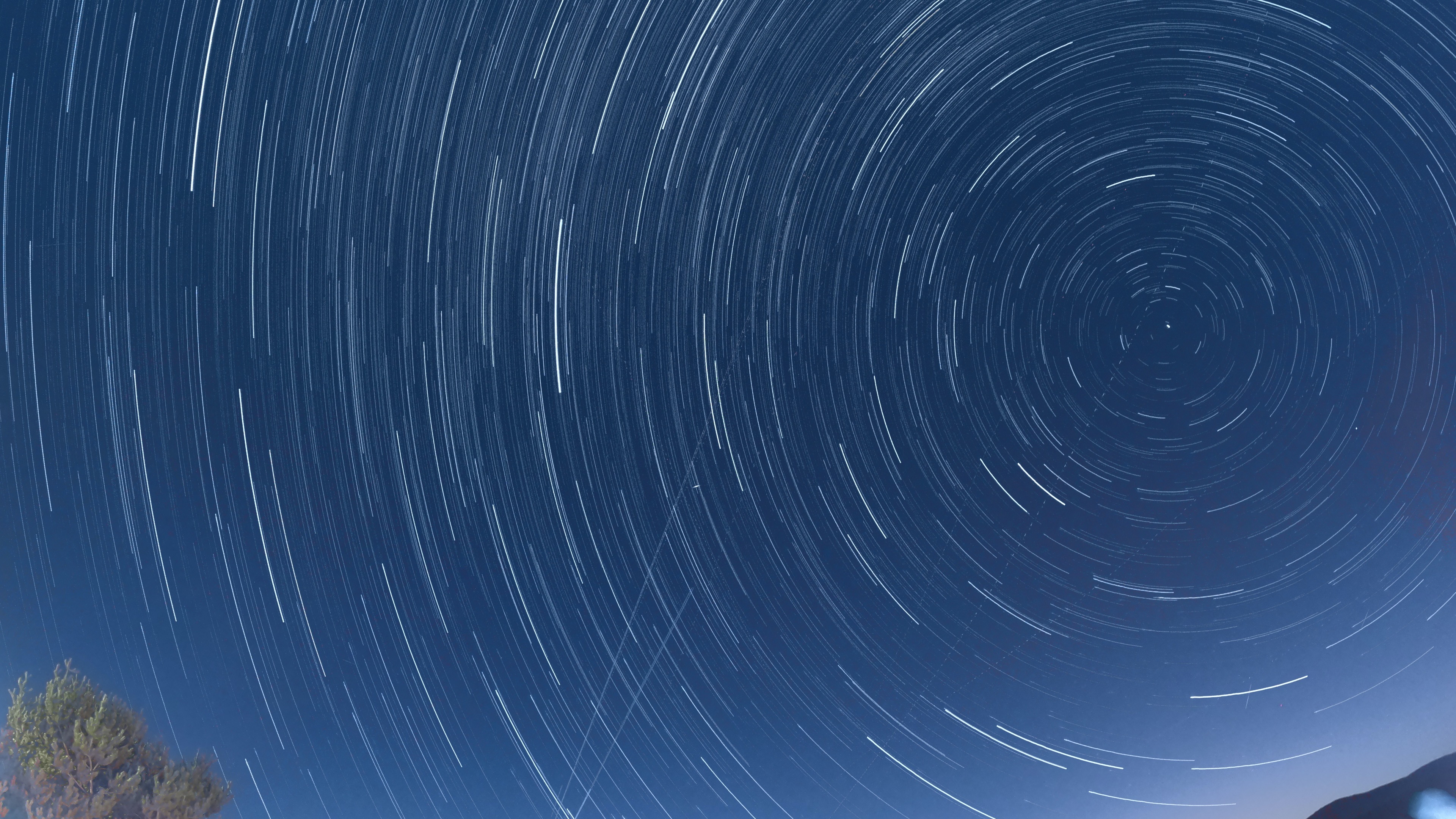 Star trails are visible in a long-exposure photograph circling the North Star. Streaks of meteors are visible passing through the pattern.