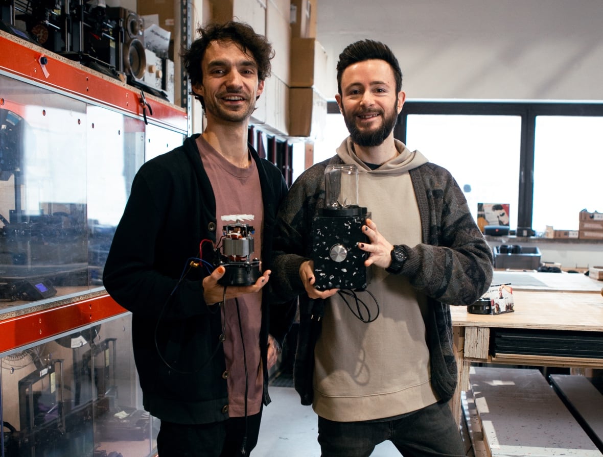 Two people stand side by side, holding blenders.