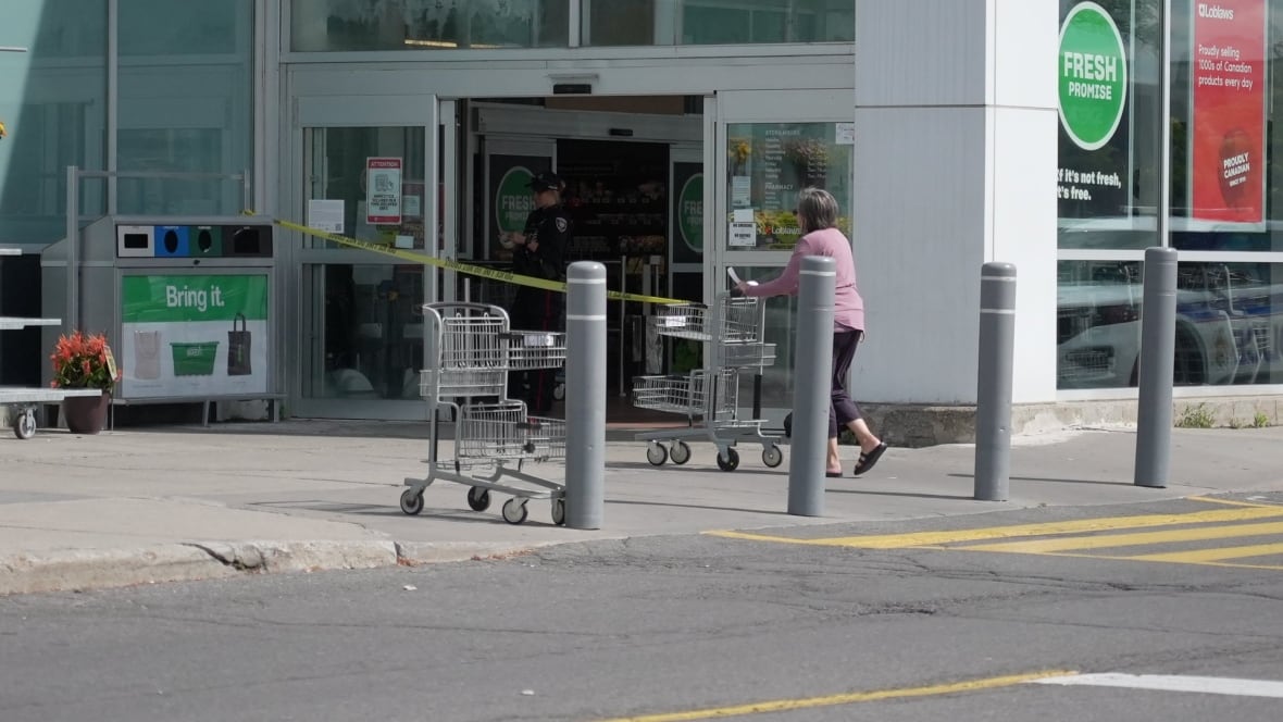 A police officer stands behind police tape at the front of a grocery store.