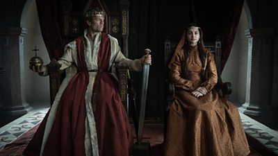 Actor James Norton, playing Harold, is sitting on a throne with a sword on his left hand. He faces left at actress Indy Lewis, playing Margaret, who is sitting on a throne next to him facing forward. The scene is set in a castle.