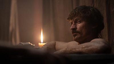 William, Duke of Normandy (Nikolaj Coster-Waldau) is offset right in the image. He is staring off into the distance while a candle burns next to him