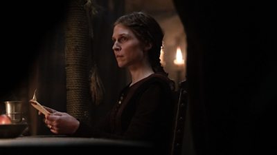 Matilda (Clémence Poésy) is central in the image in a dimly lit room. She is holding paper which is on fire as she stares into the distance.