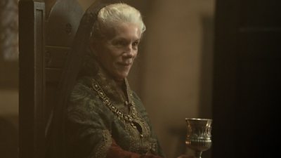 Lady Emma (Juliet Stevenson) is central in the image, sitting on a throne with a chalice in her left hand. She is staring off into the distance.