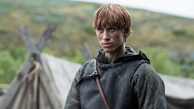 Tostig (Luther Ford) is central in the image looking forward. There are huts in the background