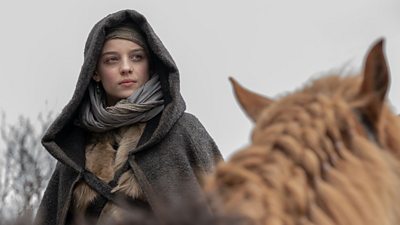 Queen Gunhild (Bo Bragason) is sitting on a horse facing forcward wrapped in a cloak