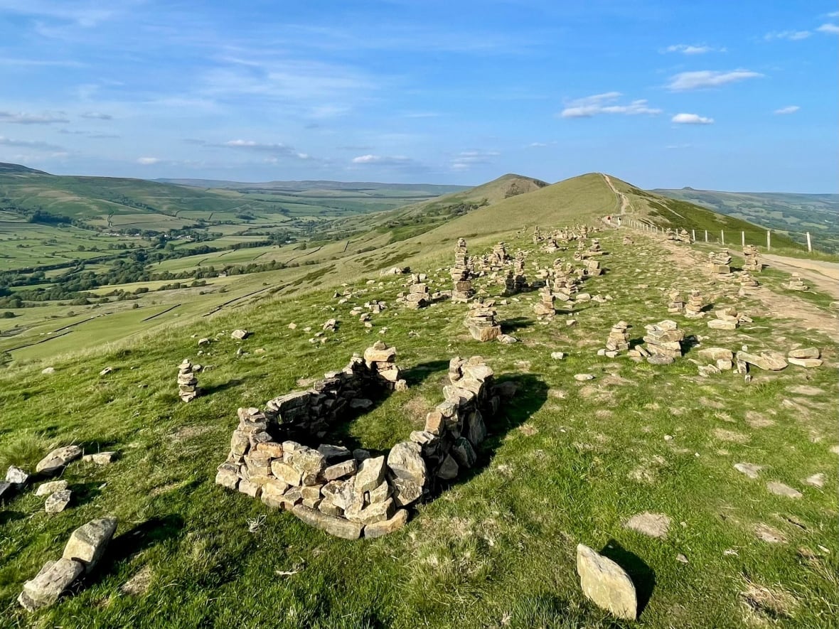 A rolling green hillside covered with stacked rocks