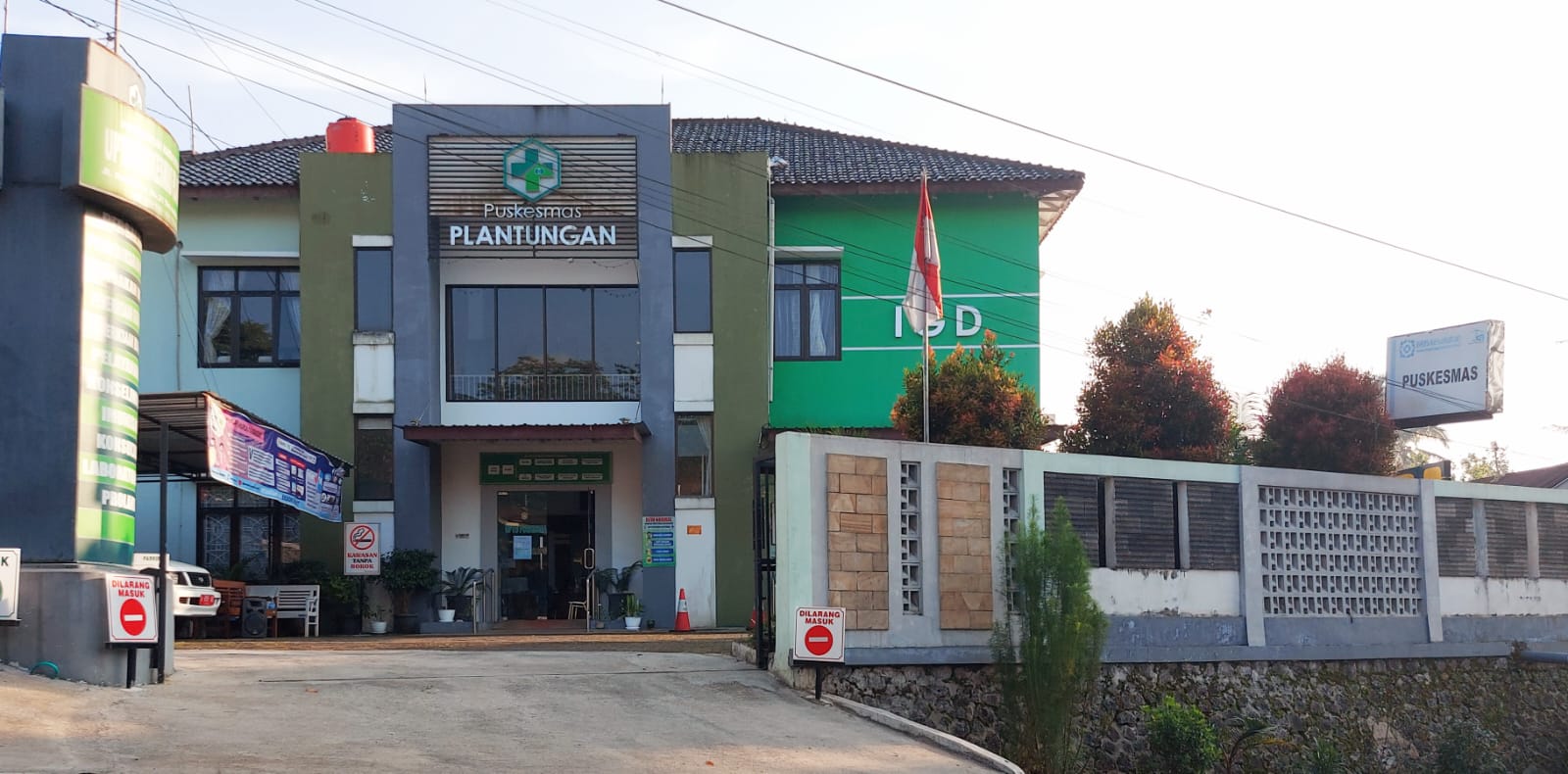 Front entrance of Puskesmas Plantungan, a green and white healthcare facility with its name on a sign, an Indonesian flag