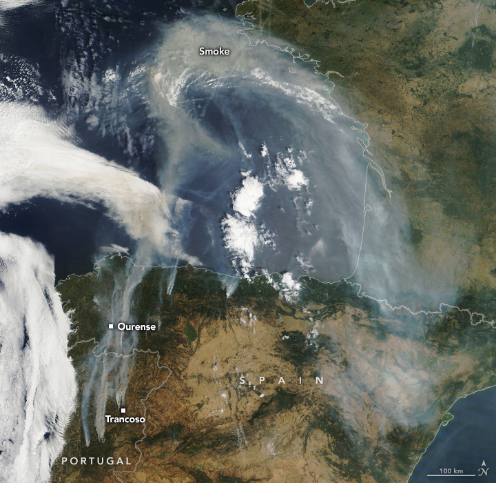 A satellite image shows plumes of brown smoke pouring from Spain and Portugal, pictured in the bottom third of the scene. The smoke billows toward the top of the image over blue water and then circles back over the brown and green land.