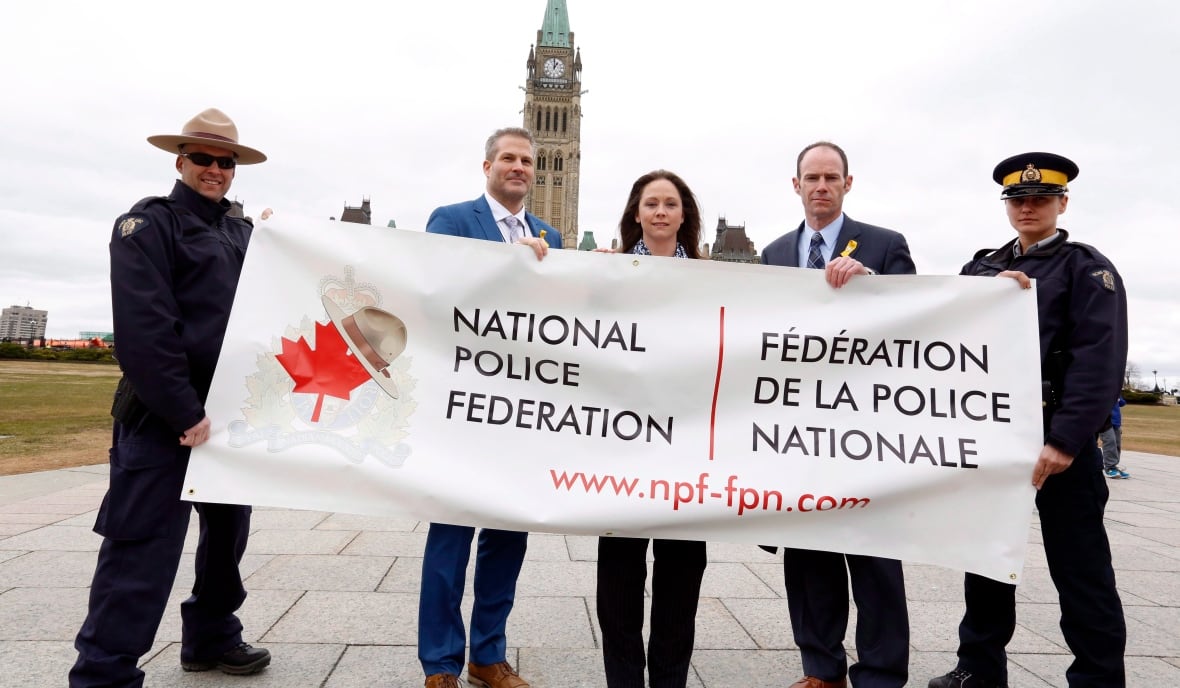 Members of the RCMP hold a banner on Parliament Hill, Wednesday April 12, 2017. From left to right Constable Eric Decoste, Dennis Miller, Lorette Jones, Brian Sauve and Maria Pikus. Mounties are protesting wages, staffing levels and working conditions by removing the yellow stripes running down the sides of their pants.