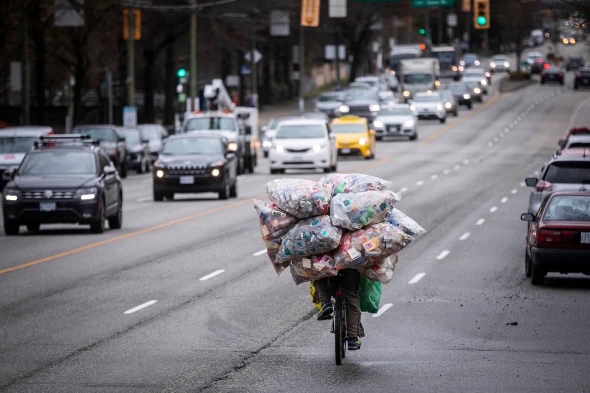 A man carries multiple bags of recyclable bottles and cans while riding his bike in Vancouver, British Columbia, on Tuesday, March 1, 2022.