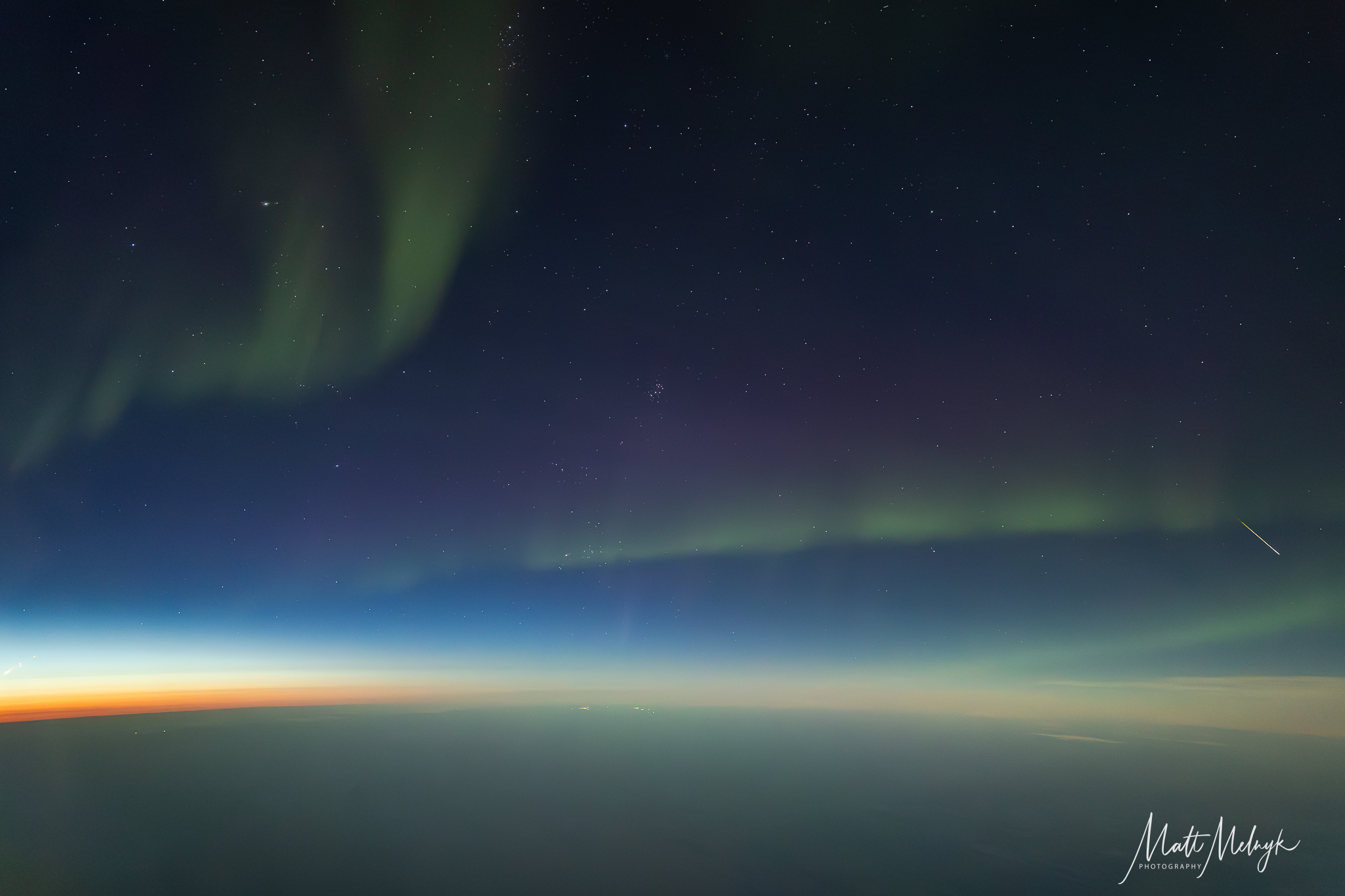 A lone meteor is pictured streaking through a sky wreathed in a twisting green aurora in a scene shot from an airplane. The curvature of Earth is visible below.