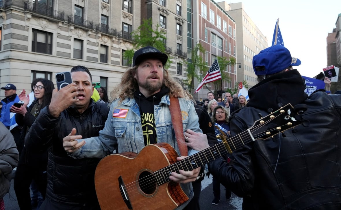 A man with long hair holds a guitar during a rally.