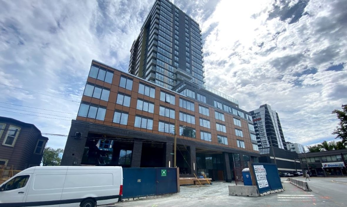 A high-rise building is seen from below, with construction equipment scattered around the base