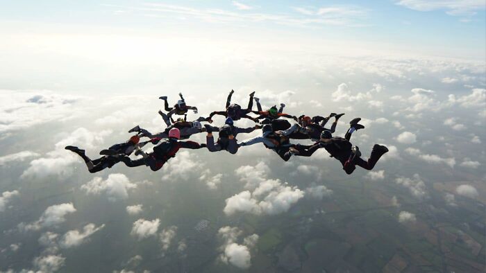 Group of skydivers in formation above clouds during a high-altitude jump capturing the thrill of a 15,500-ft fall.