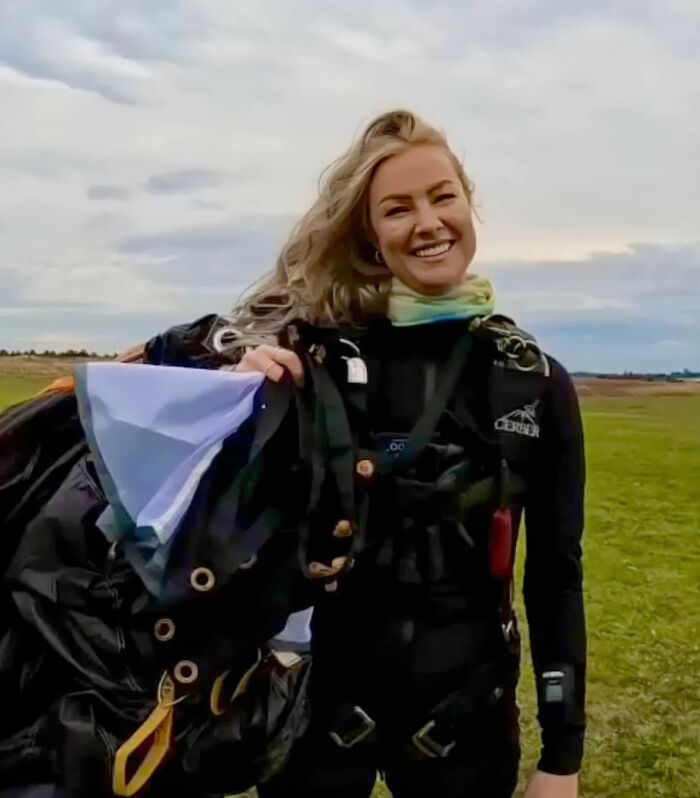 Woman in skydiving gear smiling outdoors after a 15,500-ft jump following a breakup, inspiring many online.