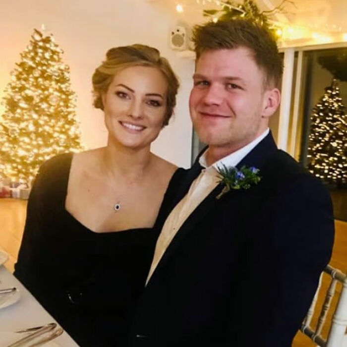 Smiling woman and man dressed formally seated at a table with Christmas trees and lights in the background.